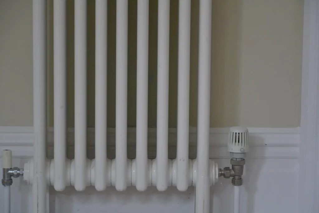 A white radiator with vertical metal bars is mounted on a wall with a temperature control valve on the side.