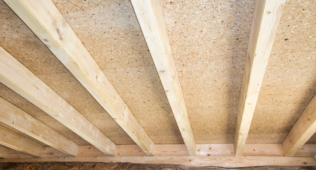 Close-up view of unfinished wooden floor joists and oriented strand board subfloor in a construction site, where using thermal paint in Surrey homes can help lower heating bills.