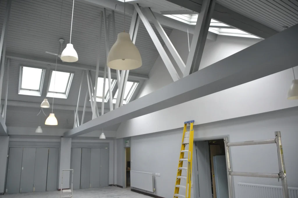 Commercial interior with high ceilings and walls being spray-painted from scaffolding