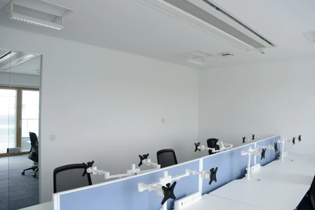 Open-plan office with desks, partition screens and repainted walls under ceiling lighting