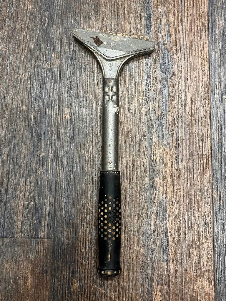 A wide steel paint scraper on a dark wooden floor