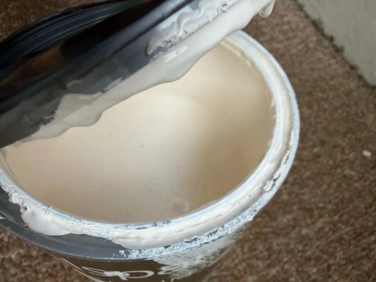 A paint kettle with a loaded brush resting on the rim, cream emulsion