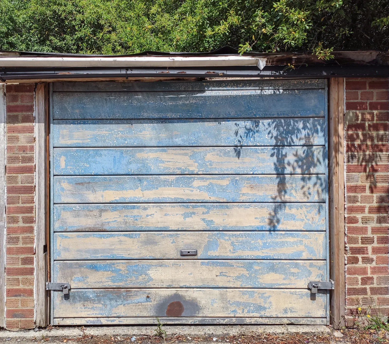 A weathered blue garage door with flaking paint set in a brick wall