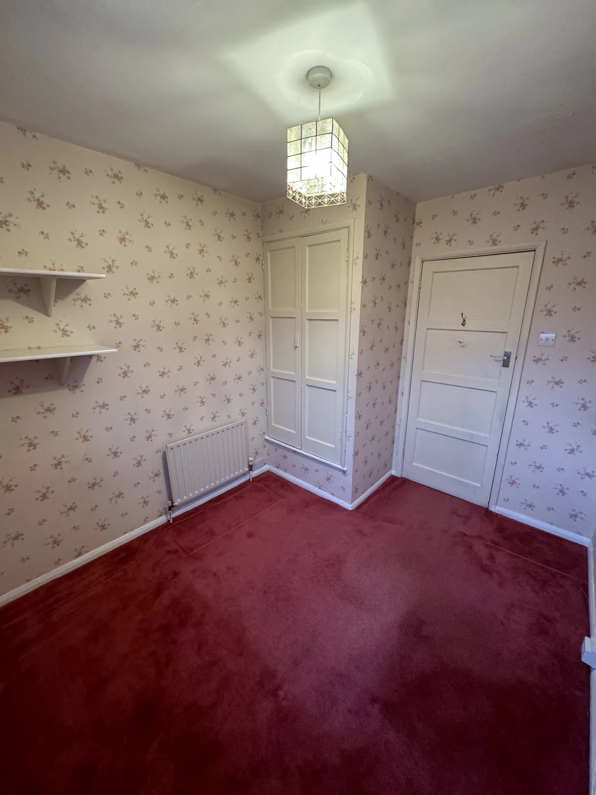 An empty room with patterned wallpaper, a white door and a red carpet, ready for redecoration