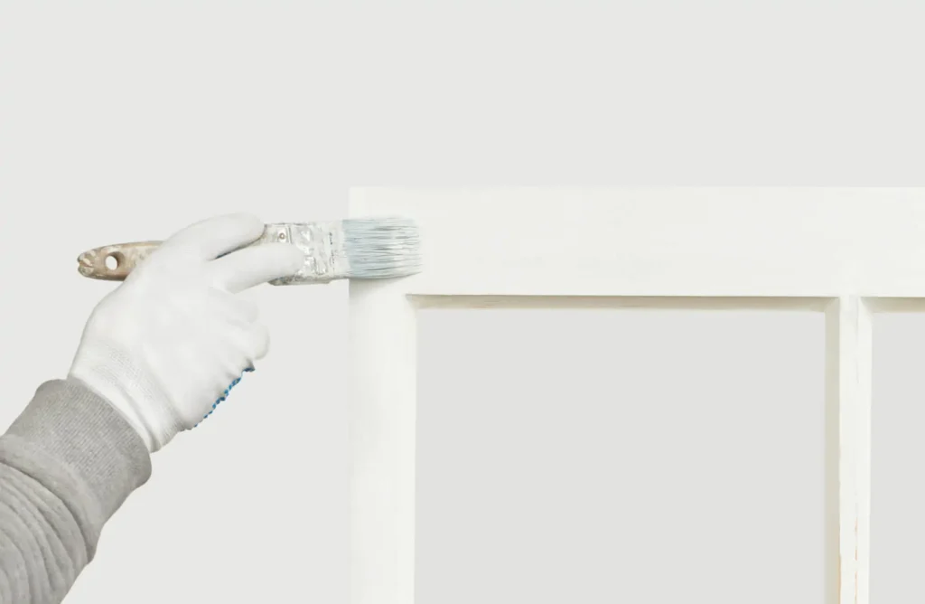 Wooden window frame being hand-painted white with a brush