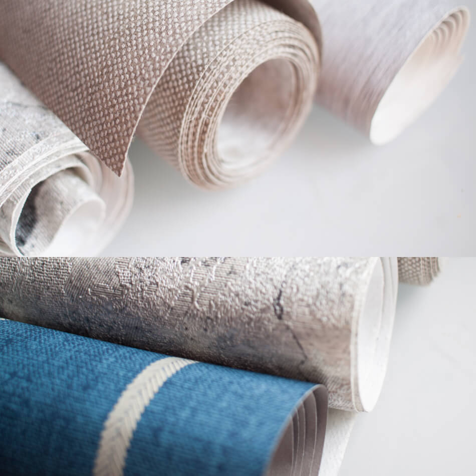 Close-up of various rolls of textured wallpaper in neutral and blue tones, laid out on a flat surface, ready to transform spaces with the touch of experienced wallpaper hangers in London.