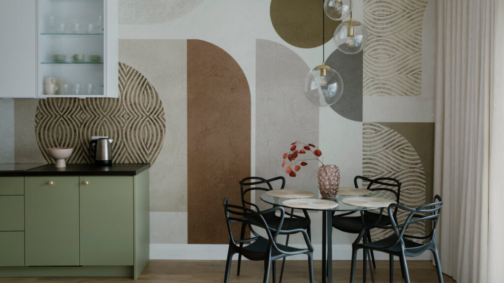 A modern kitchen and dining area with green cabinets, a round glass table set for four, black chairs, and geometric patterned wallpaper in wet rooms creates a stylish look in neutral tones.