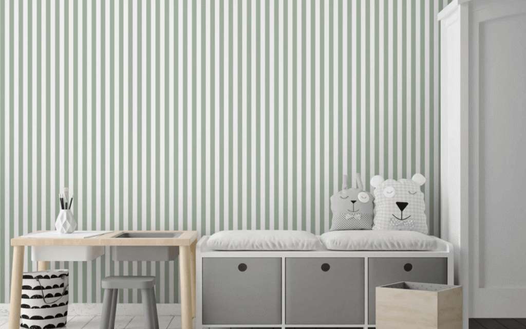 Children's room with a striped wall reflecting the latest wallpaper trends, a wooden table and stool, a bench with animal face cushions, storage cubes, and a white wardrobe.